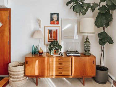 Beige pleated lampshade on a wood bracket, eclectic art, plant, vintage accents, record player, and wood sideboard